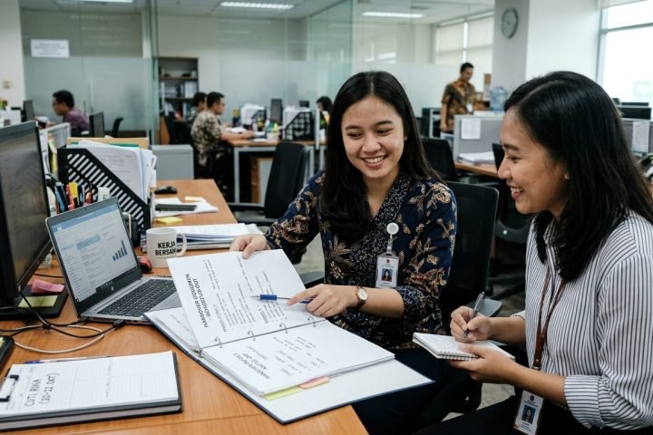 Karyawan baru mendiskusikan dokumen handover tugas bersama rekan kerja sebelum mengambil cuti